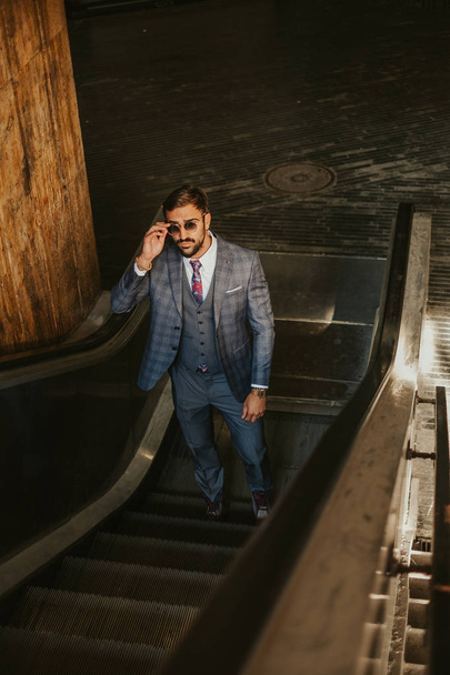 Серьезный бизнесмен поднимается на эскалатор, держа пение
 - Фото, изображение