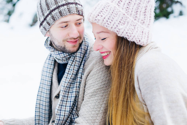 the guy looks at the girl who sincerely smiles and her eyes is closed. they sit on the snow in warm clothes - Photo, Image