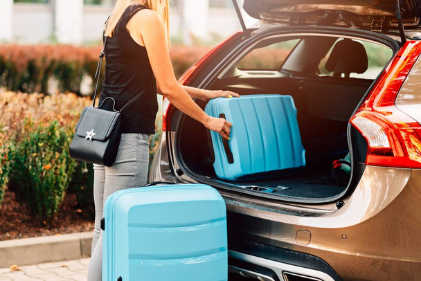 Donna che carica due valigie di plastica blu sul bagagliaio dell'auto. Preparazione per il viaggio
 - Foto, immagini