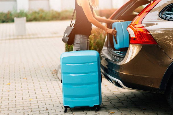 Mulher carregando duas malas de plástico azul no porta-malas do carro. Preparação para a viagem
 - Foto, Imagem