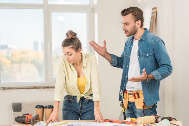 emotional young man with toolbelt gesturing and quarreling with girlfriend during house repair - Photo, Image