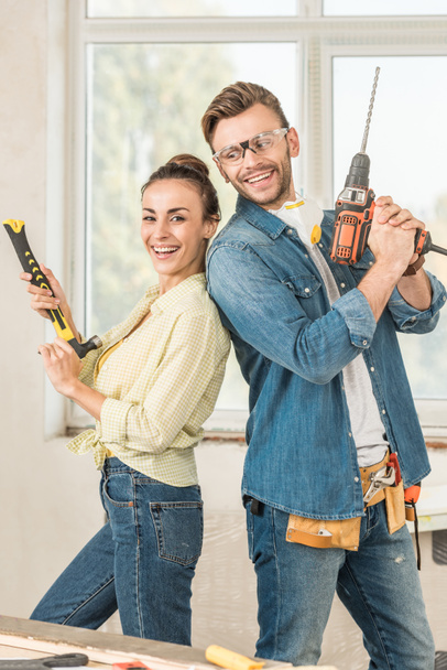 happy young couple holding hammer and electric drill during house repair - Photo, Image