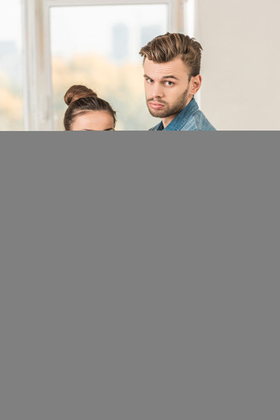 Aufgebrachter junger Mann umarmt enttäuschte Freundin und blickt während Hausreparatur in die Kamera - Foto, Bild