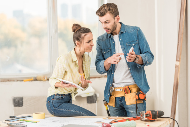 young couple using digital devices while making repairment in new apartment - Fotoğraf, Görsel