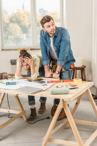 joven pareja molesta inclinada a la mesa con herramientas durante la reparación
 - Foto, imagen