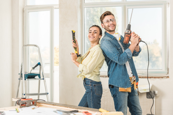 happy young couple holding tools and smiling at camera during house repair - 写真・画像