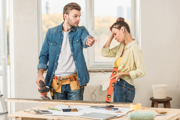 emotional young couple holding tools and quarreling during renovation - Photo, Image