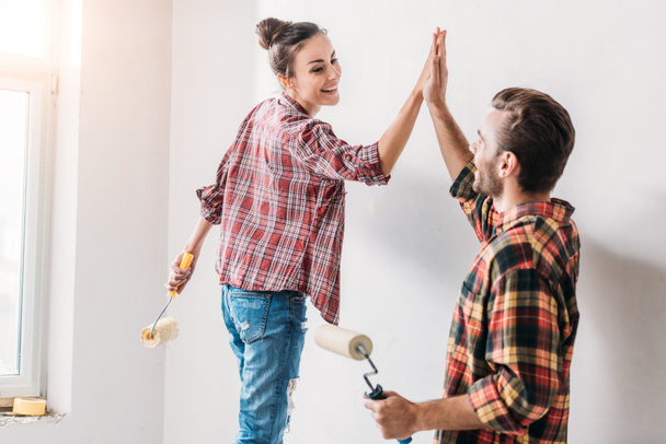 feliz joven pareja dando alta cinco mientras que la pintura de la pared en el nuevo apartamento
 - Foto, Imagen
