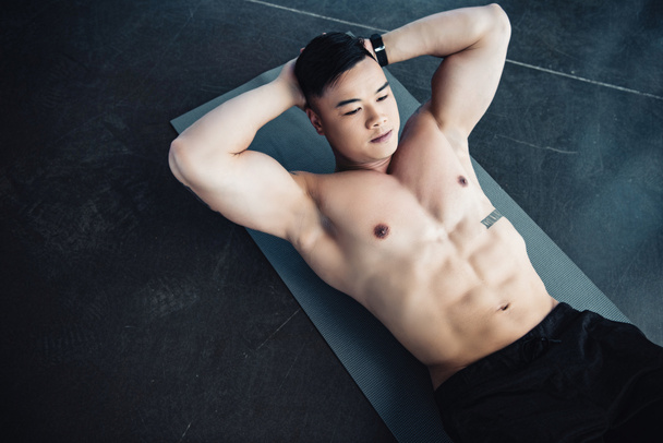 young asian sportsman with bare chest doing abs exercise on fitness mat at gym - Photo, image