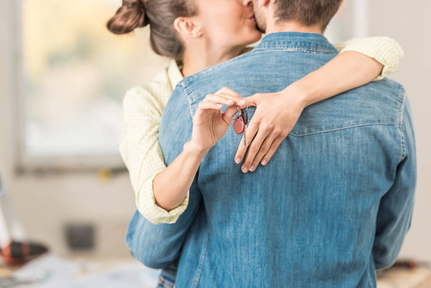 обрізаний знімок щасливої молодої жінки, що обіймає і цілує чоловіка, тримаючи ключ від нової квартири
 - Фото, зображення