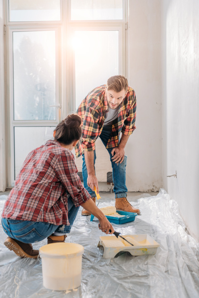 young couple in checkered shirts holding paint rollers and painting wall - Photo, Image