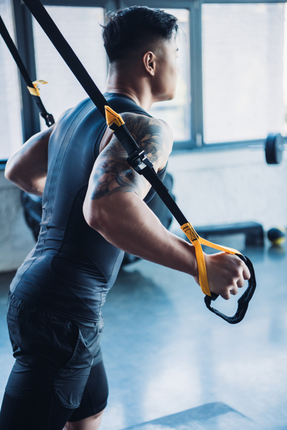 side view of young muscular sportsman training with resistance bands in gym - Foto, afbeelding