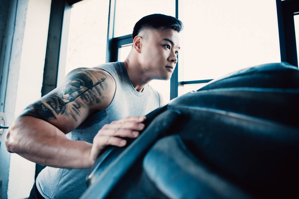 handsome young sportsman flipping heavy tire at gym - Photo, Image