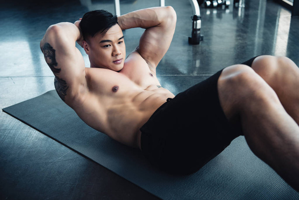 apuesto joven deportista con el pecho desnudo haciendo ejercicios abdominales en la alfombra de fitness en el gimnasio
 - Foto, Imagen