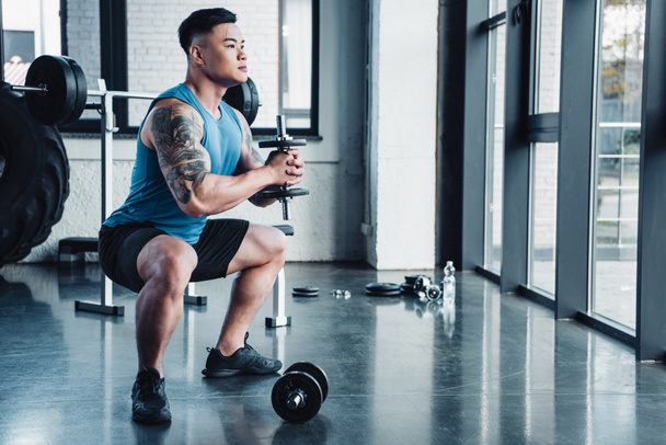 concentrated young sportsman exercising with dumbbells in gym - Photo, Image