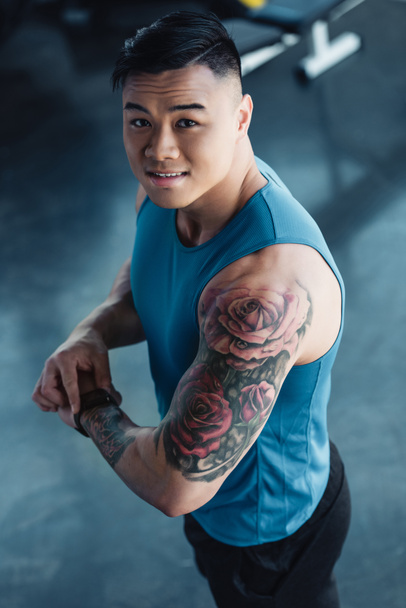 young tattooed asian sportsman at gym looking at camera - Foto, imagen