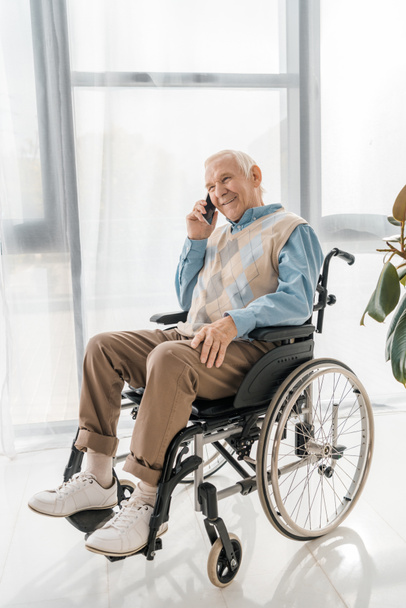 senior smiling man sitting in wheelchair and talking on smartphone in nursing home - Photo, image