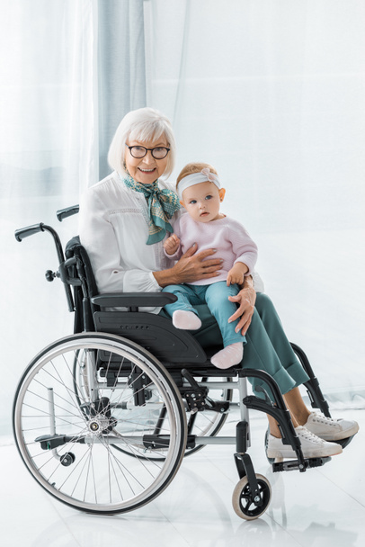 smiling grandmother in wheelchair holding small granddaughter - Φωτογραφία, εικόνα