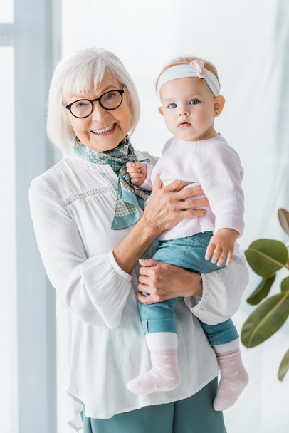 cheerful grandmother in glasses holding small granddaughter - Photo, Image