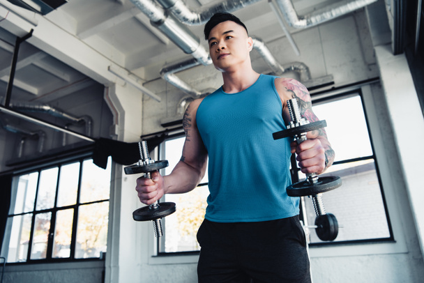 concentrated young sportsman exercising with dumbbells in gym - 写真・画像