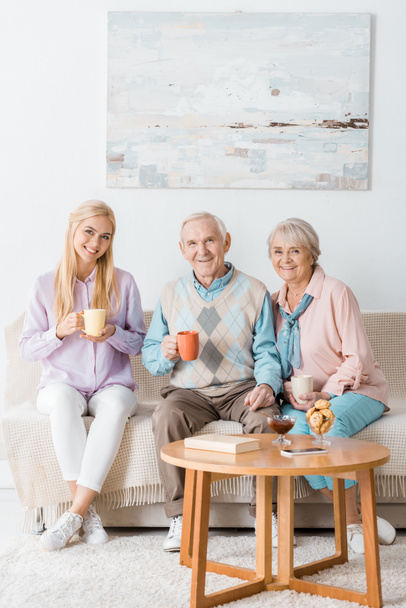 ソファーに座っていた先輩の両親と一緒にお茶を飲む若い女性 - 写真・画像