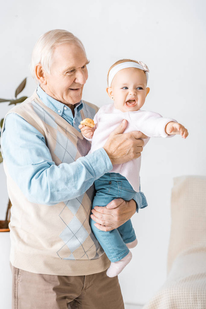 старший улыбающийся дедушка держит внучку малыша с печеньем
 - Фото, изображение