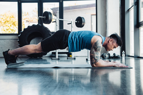 side view of young sportsman doing plank exercise at gym - Foto, immagini