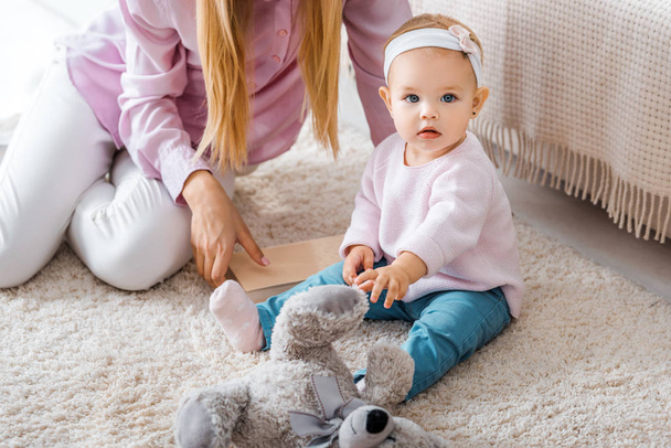 mother sitting on carpet with little daughter and playing with toy - Photo, Image