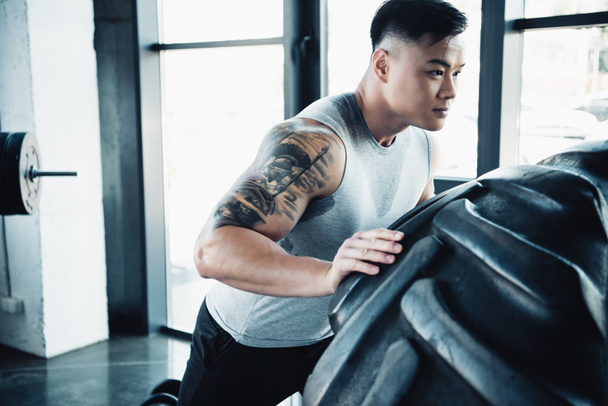 focused young sportsman flipping heavy tire at gym - Photo, Image