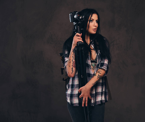 Seducente ragazza tatuata che indossa una camicia a quadri sbottonata ragazza in posa con una fotocamera
. - Foto, immagini