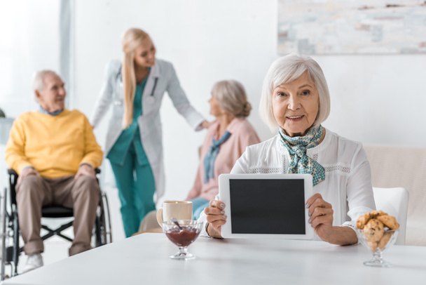 mujer mayor sosteniendo tableta digital en el hogar de ancianos con personas mayores y médico de fondo
 - Foto, Imagen