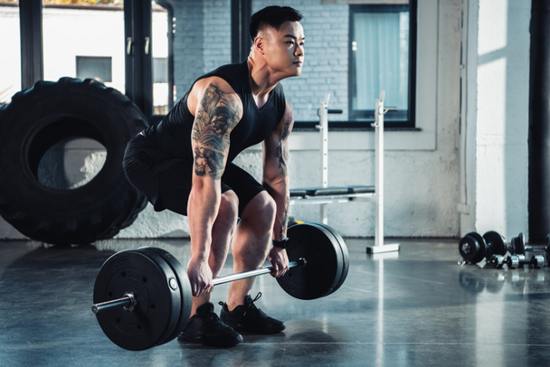muscular tattooed sportsman training with barbell at gym - Photo, Image