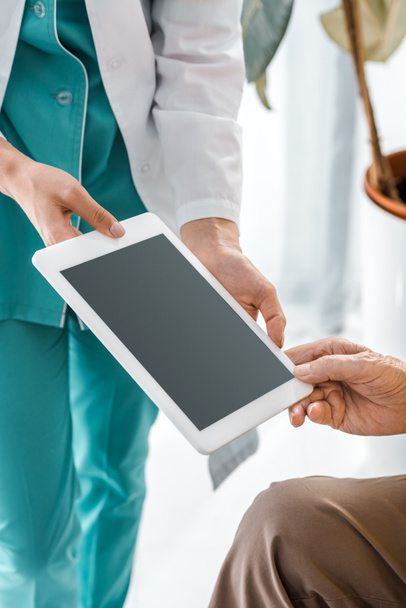 close up on doctor and senior patient hands holding digital tablet with blank screen - Fotó, kép