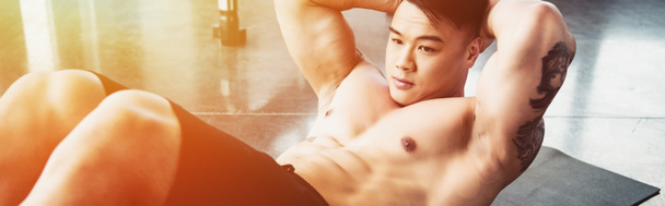young asian sportsman doing abs exercise on fitness mat at gym in sunlight - Foto, imagen