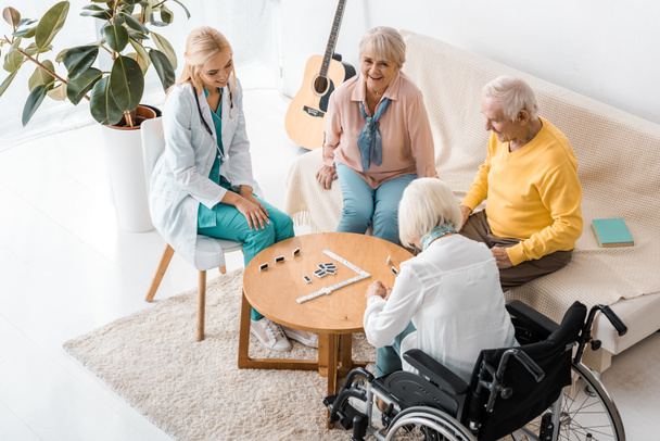 enfermera joven jugando al dominó con pacientes mayores en un hogar de ancianos
 - Foto, imagen