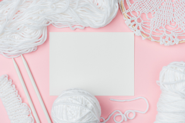 plat lag met wit garen, breinaalden en blanco papier op roze achtergrond - Foto, afbeelding