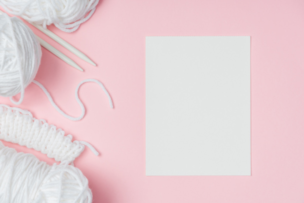deitado plano com fios brancos, agulhas de tricô e papel em branco sobre fundo rosa
 - Foto, Imagem