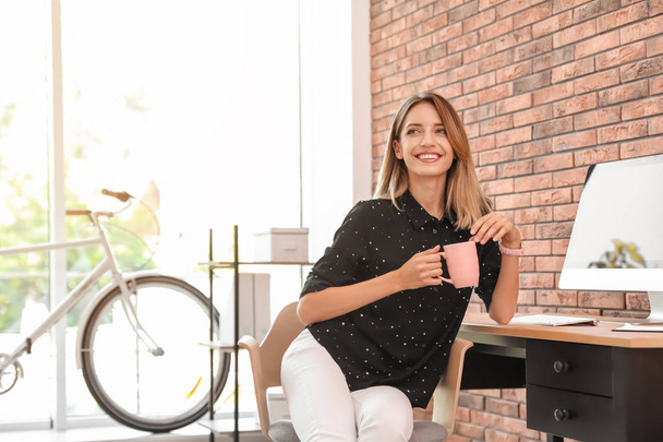 Happy young businesswoman with cup of coffee enjoying peaceful moment at workplace - Foto, imagen