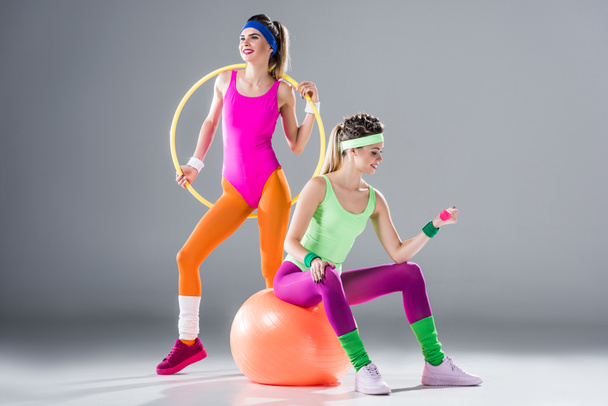 smiling sporty girls training with hula hoop, dumbbell and fit ball on grey - Photo, Image
