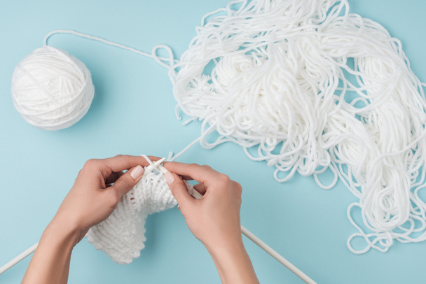 partial view of woman with white yarn and knitting needles knitting on blue backdrop - Foto, Imagem