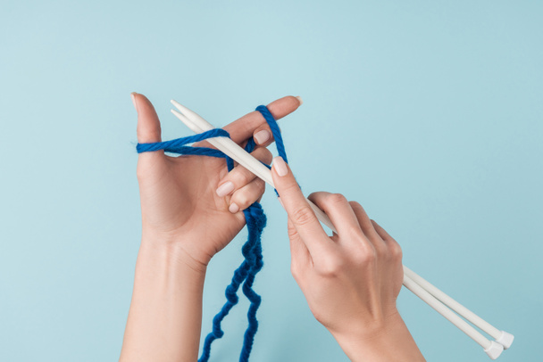 partial view of woman with blue yarn and white knitting needles knitting on blue backdrop - Photo, Image