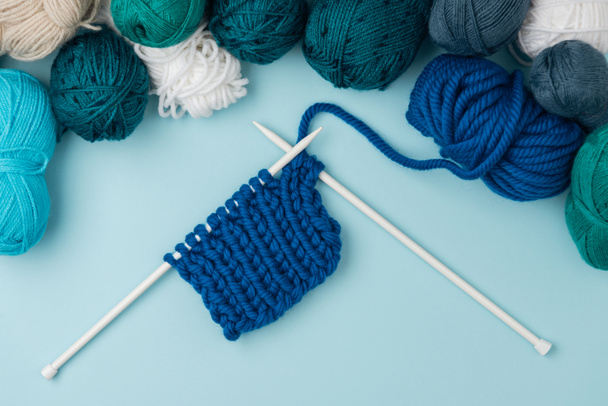 top view of arranged yarn clews and white knitting needles on blue background  - Foto, Imagem