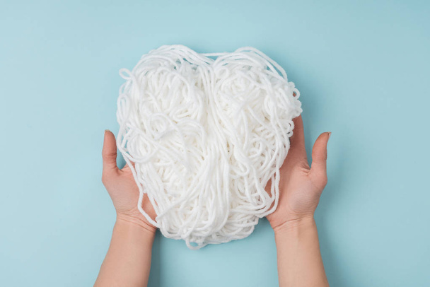 partial view of woman holding white yarn for knitting in hands on blue background - Photo, Image