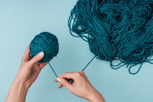 partial view of woman rolling yarn ball on blue background - Fotó, kép