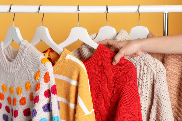 Woman choosing sweater on rack against color background, closeup - Photo, image