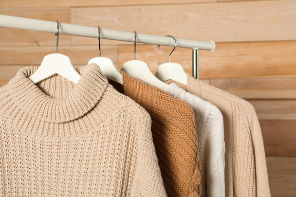 Collection of warm sweaters hanging on rack against wooden background - Photo, image