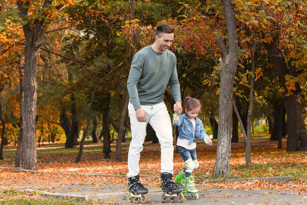 Young father and his daughter roller skating in autumn park - Foto, imagen