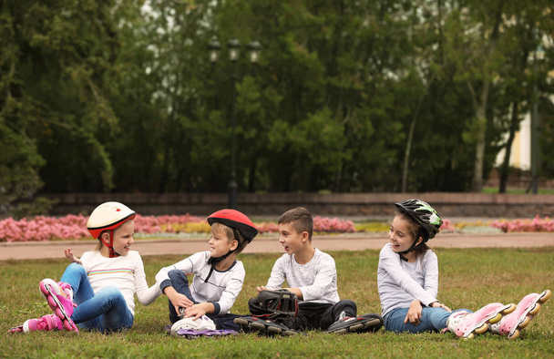 Rullaluistelijat istuvat nurmikolla puistossa.
 - Valokuva, kuva