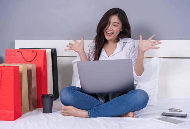 χαρούμενη γυναίκα χρησιμοποιεί το φορητό υπολογιστή για online αγορές σε ένα κρεβάτι - Φωτογραφία, εικόνα