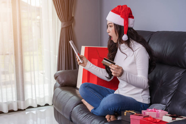 surprised woman in santa hat shopping online for Christmas gift with digital tablet in the living room - Zdjęcie, obraz